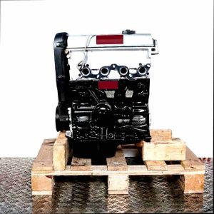 Side view of the ALM engine on a wooden pallet against a white background. The engine, featuring a light upper and dark lower section, is positioned vertically.