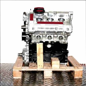 Side view of an AQD engine on a wooden pallet against a white background. The engine block is black, with silver-colored components.
