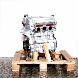 K10C car engine on a wooden pallet against a white background. Side view of the engine, vertically oriented.